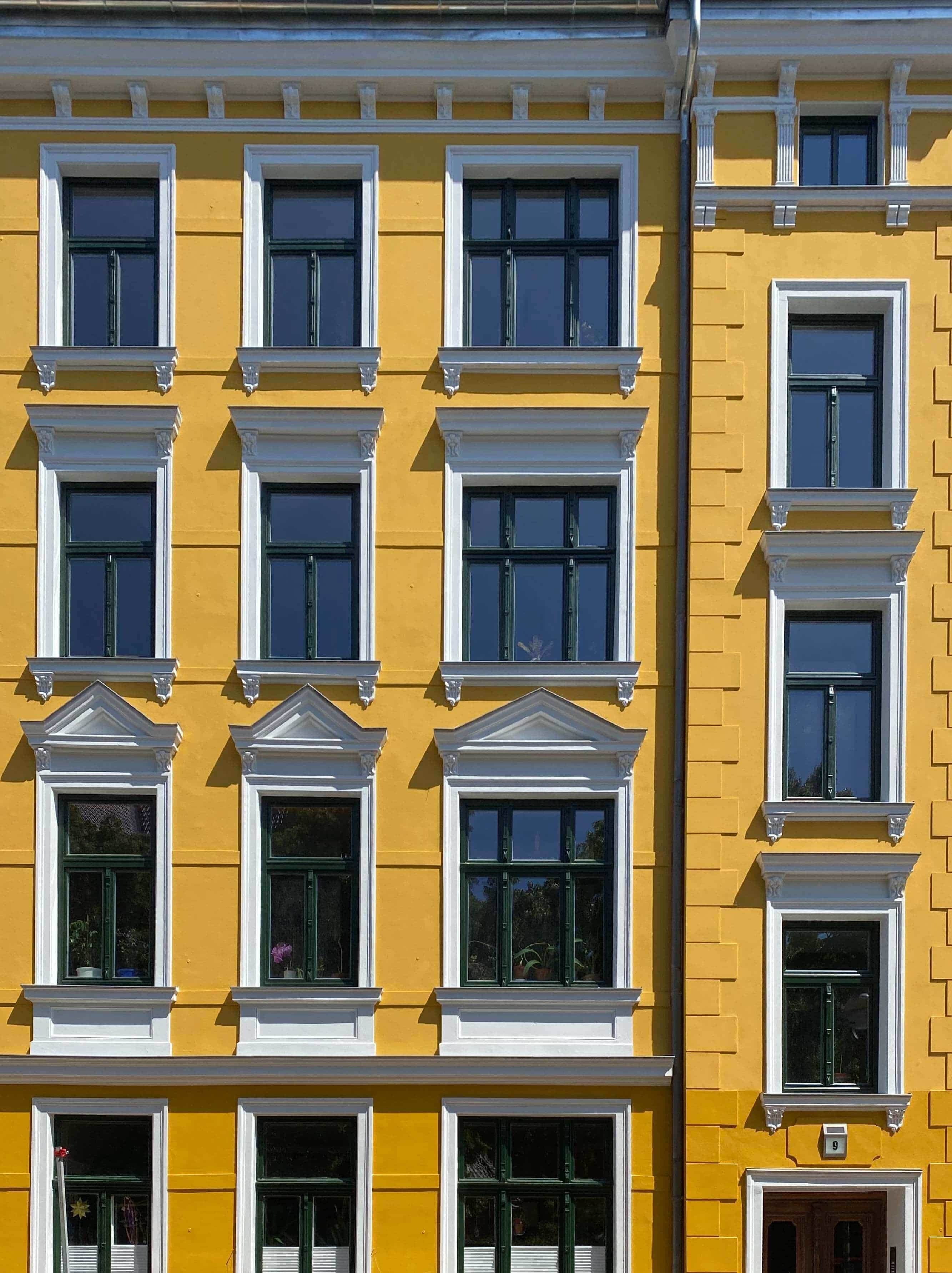 gelbe denkmalgeschützte Fassade mit Stuckarbeiten in weiß und dunkelgrünen Fenstern